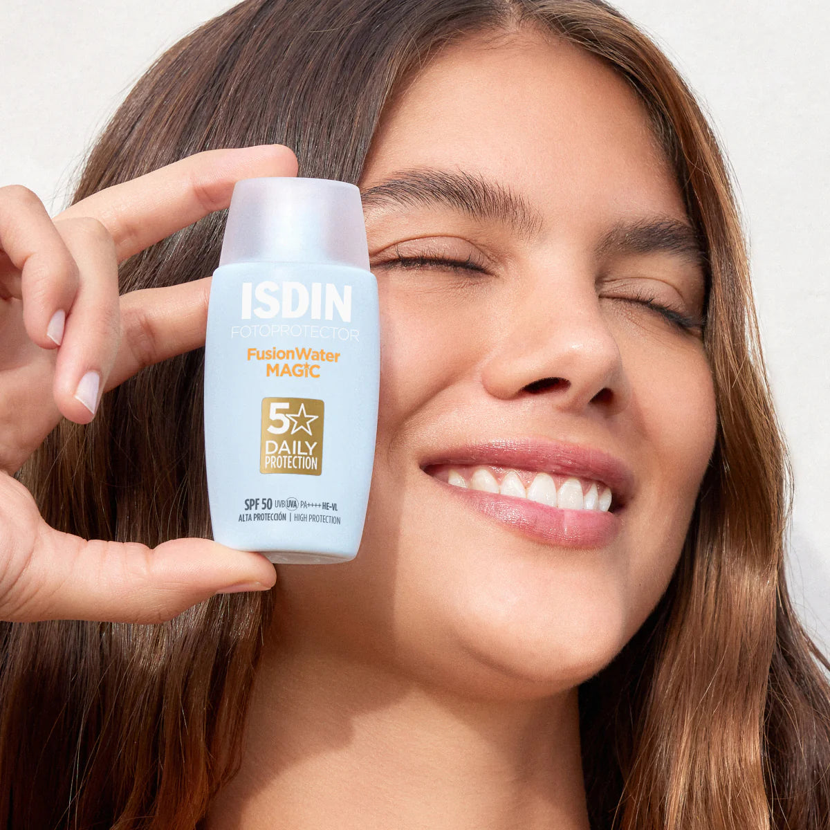 Woman holding ISDIN Fusion Water Magic sunscreen bottle close to her face.