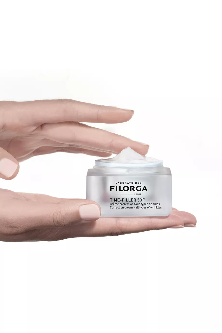 Hand holding a white jar of Filorga cream against a white background
