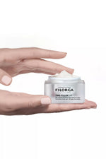 Hand holding a white jar of Filorga cream against a white background