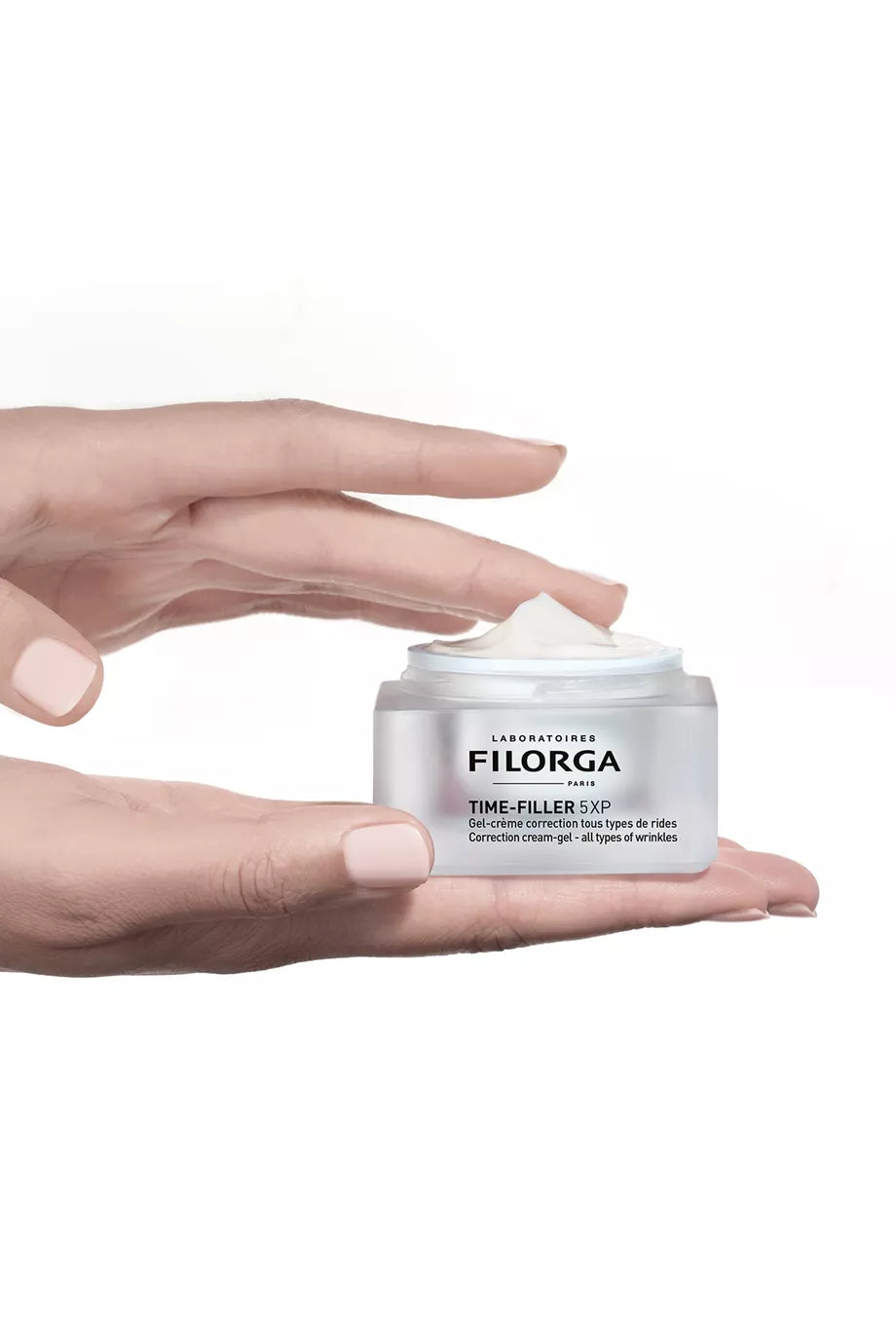 Hand holding a white jar of Filorga cream against a white background