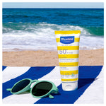 Mustela sunscreen tube with sunglasses on a beach towel by the ocean