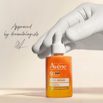 Avene ultra serum bottle held by a gloved hand on a beige background