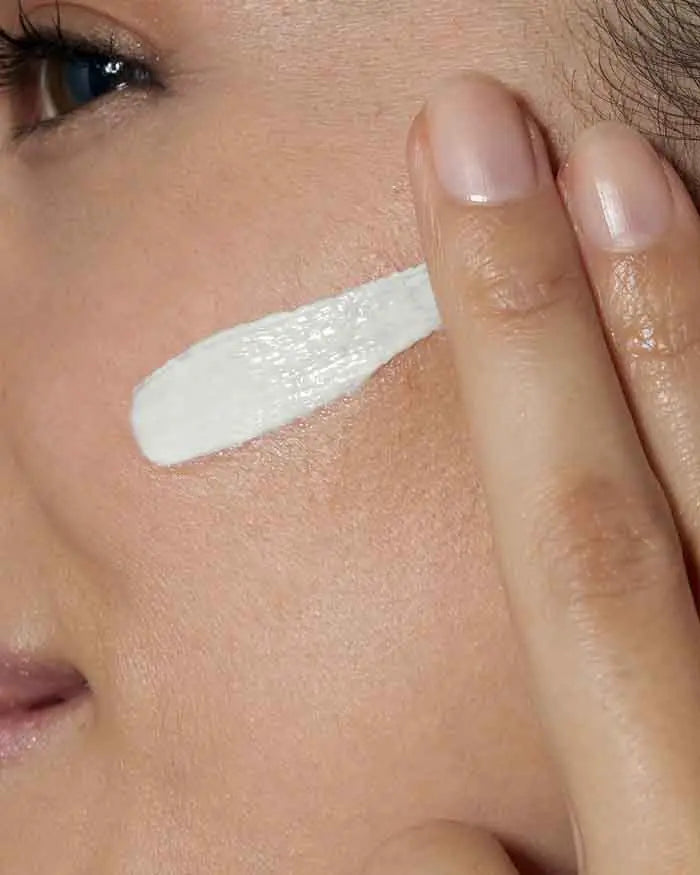 Close-up of a woman applying CeraVe face moisturizer with sunscreen t to her face with her finger.