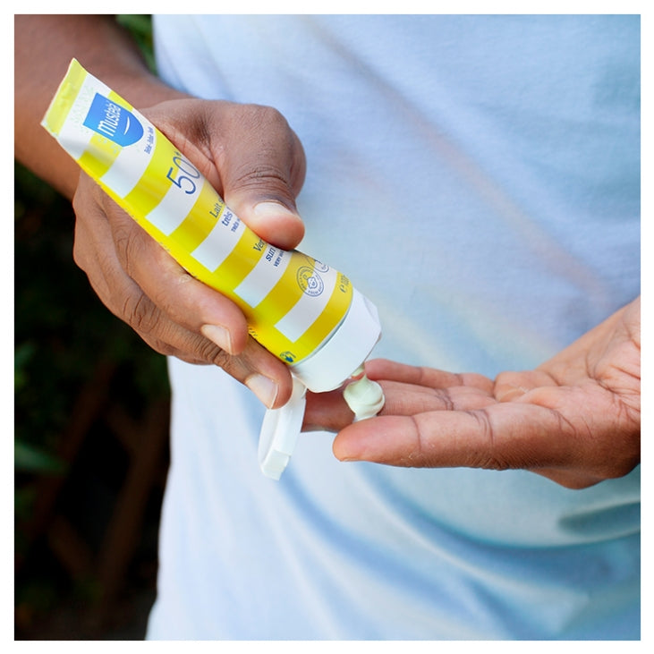 Hand applying sunscreen from a Mustela sunscreen