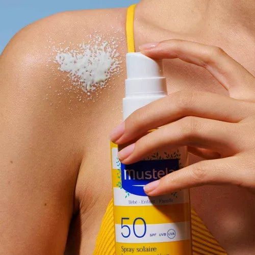 Person applying Mustela sunscreen spray to their shoulder with a clear background